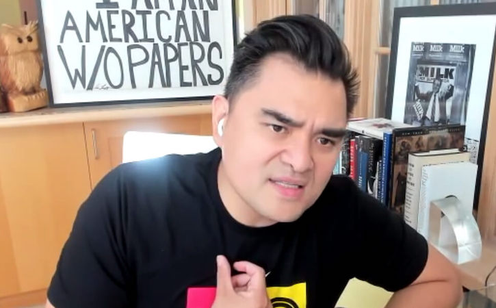 Screenshot of Jose Antonio Vargas speaking into webcam while sitting at a desk in front of a framed drawing of the text I Am An American W/O Papers