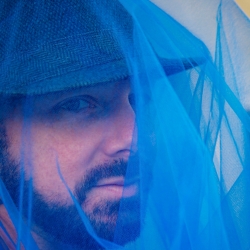 Photo of Author Miah Jeffra, with a blue gauze fabric piece obscuring their face.